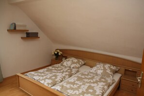 Une chambre à coucher avec un lit en bois, deux tables de chevet, une petite étagère avec quelques objets et une horloge.