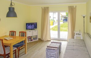 Una sala de estar con una mesa de comedor de madera, un sofá, un televisor sobre un mueble bajo y una estantería.