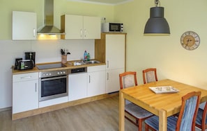 A compact kitchen with white cabinets, a microwave, a stove, and a sink. There's a wooden dining table with chairs and a wall clock. - Beautiful apartment in Boiensdorf with sauna (Boiensdorf)