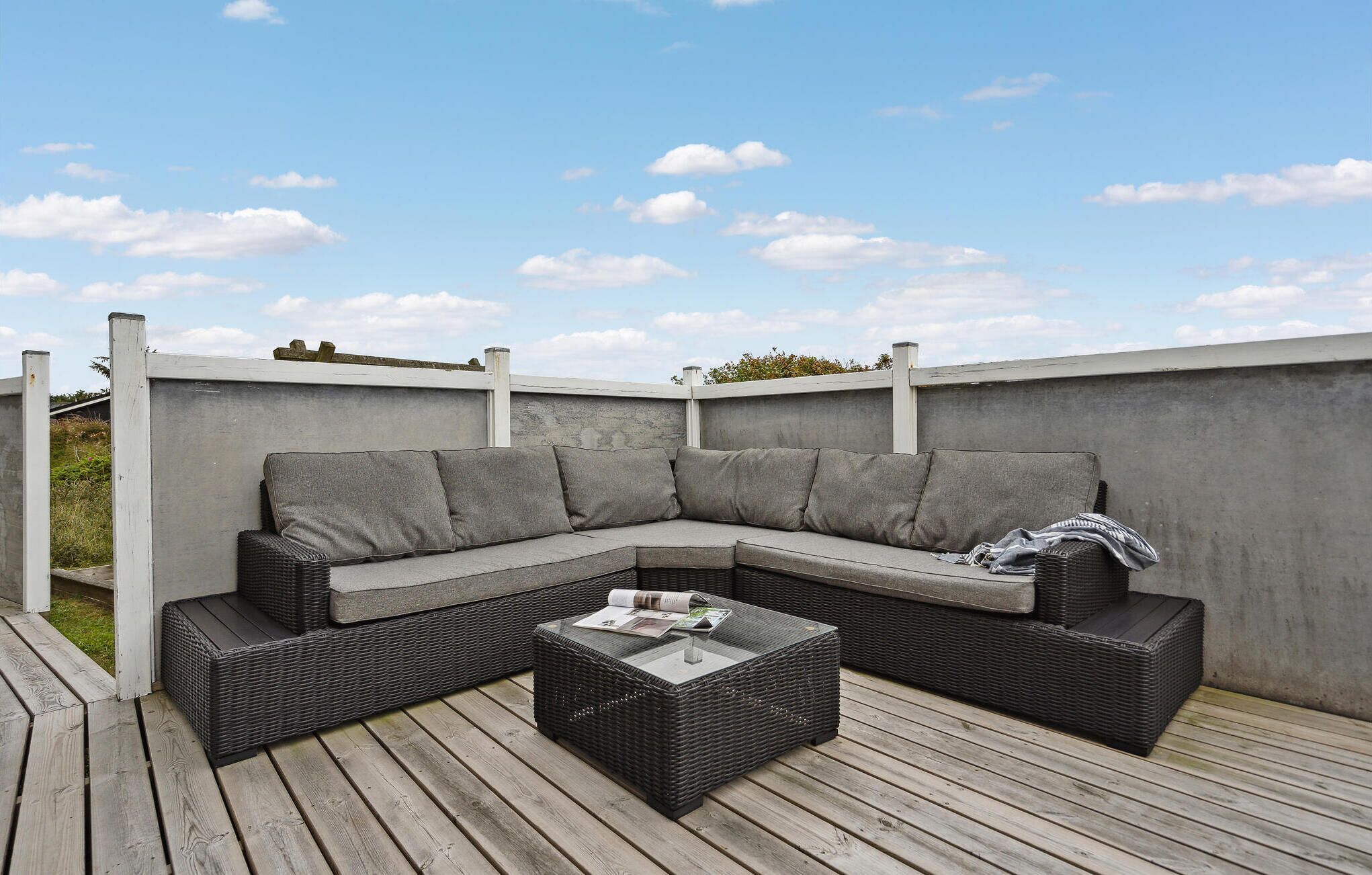 A sectional sofa with cushions and a glass-top coffee table on a wooden deck.