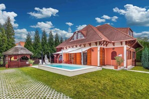 A two-story house with a swimming pool, a thatched-roof gazebo, and a well-maintained lawn.