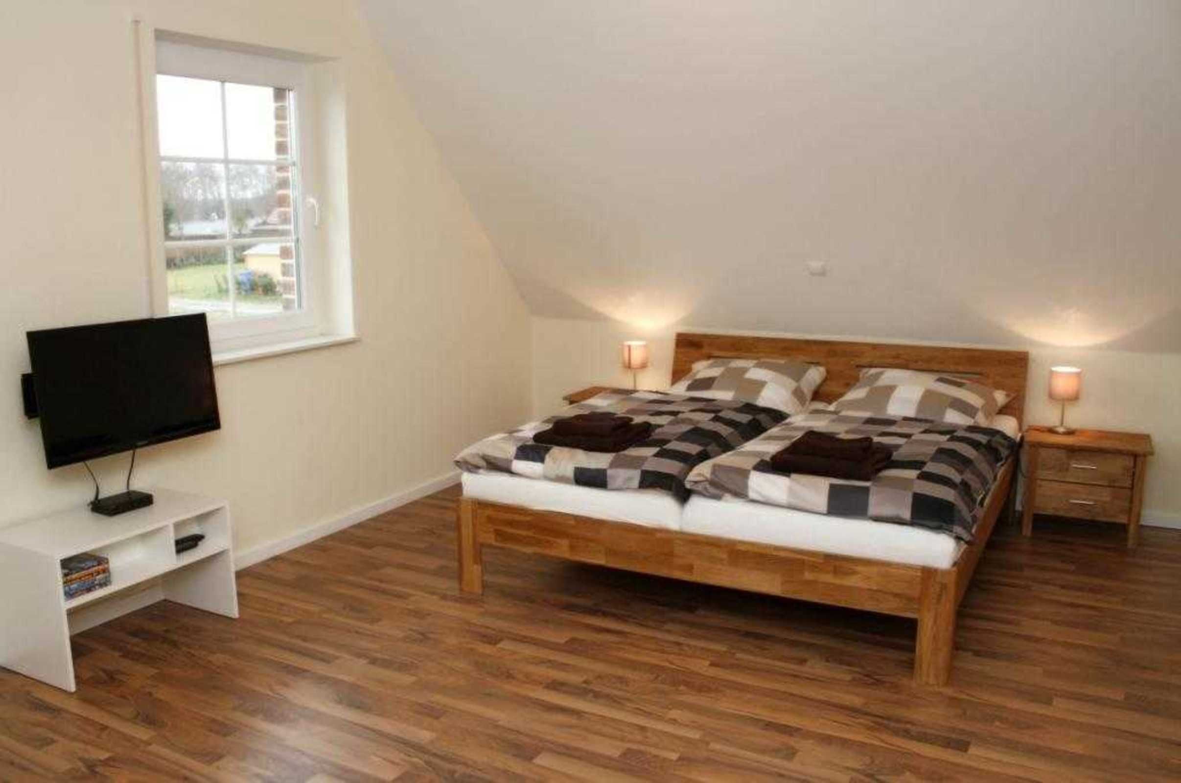 Een slaapkamer met een houten bed, een televisie op een meubel, een raam en een nachtkastje met een lamp.