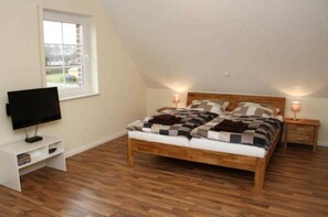 A bedroom with a wooden bed, a television on a stand, a window, and a nightstand with a lamp. - Holiday house beach pearl (Garrel)