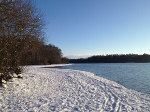 A snow-covered path leading to a body of water with trees on the left. - Holiday house beach pearl (Garrel)