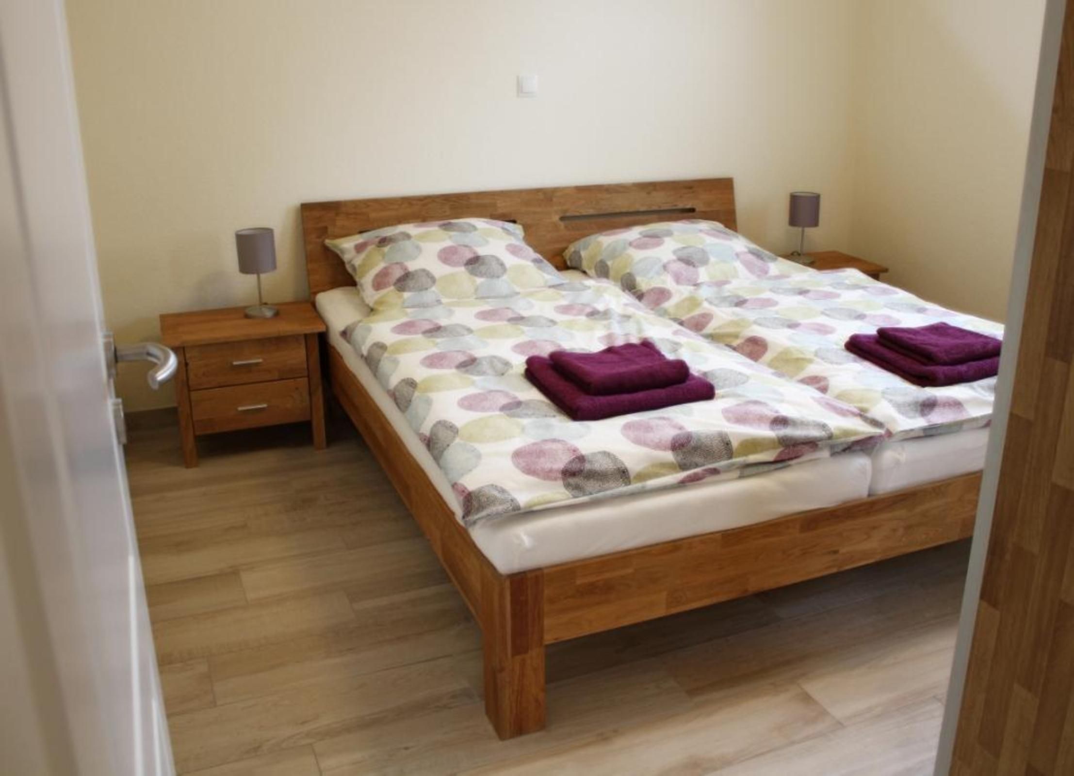 A double bed with a floral bedspread, two nightstands with lamps, and a wooden floor.
