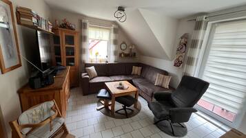 Ein Wohnzimmer mit einer Couch, einem Esstisch, einem Fernseher und einem Sessel.