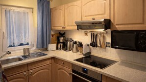 Une cuisine avec des meubles de rangement en bois, un évier en acier inoxydable, un grille-pain, une machine à café, un four à micro-ondes et une cuisinière.