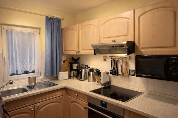A kitchen with wooden cabinets, a stainless steel sink, a toaster, a coffee maker, a microwave, and a stove.