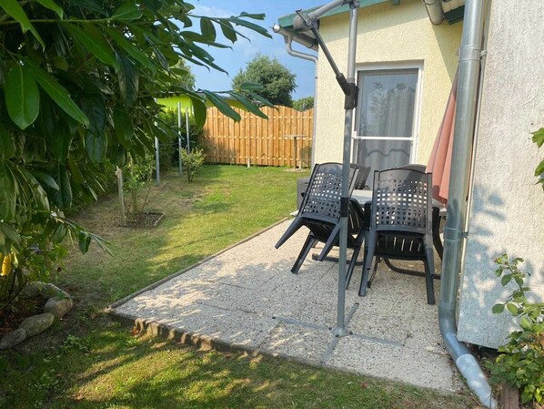 A patio with two chairs and a table, a wooden fence, and a house with a door and window.