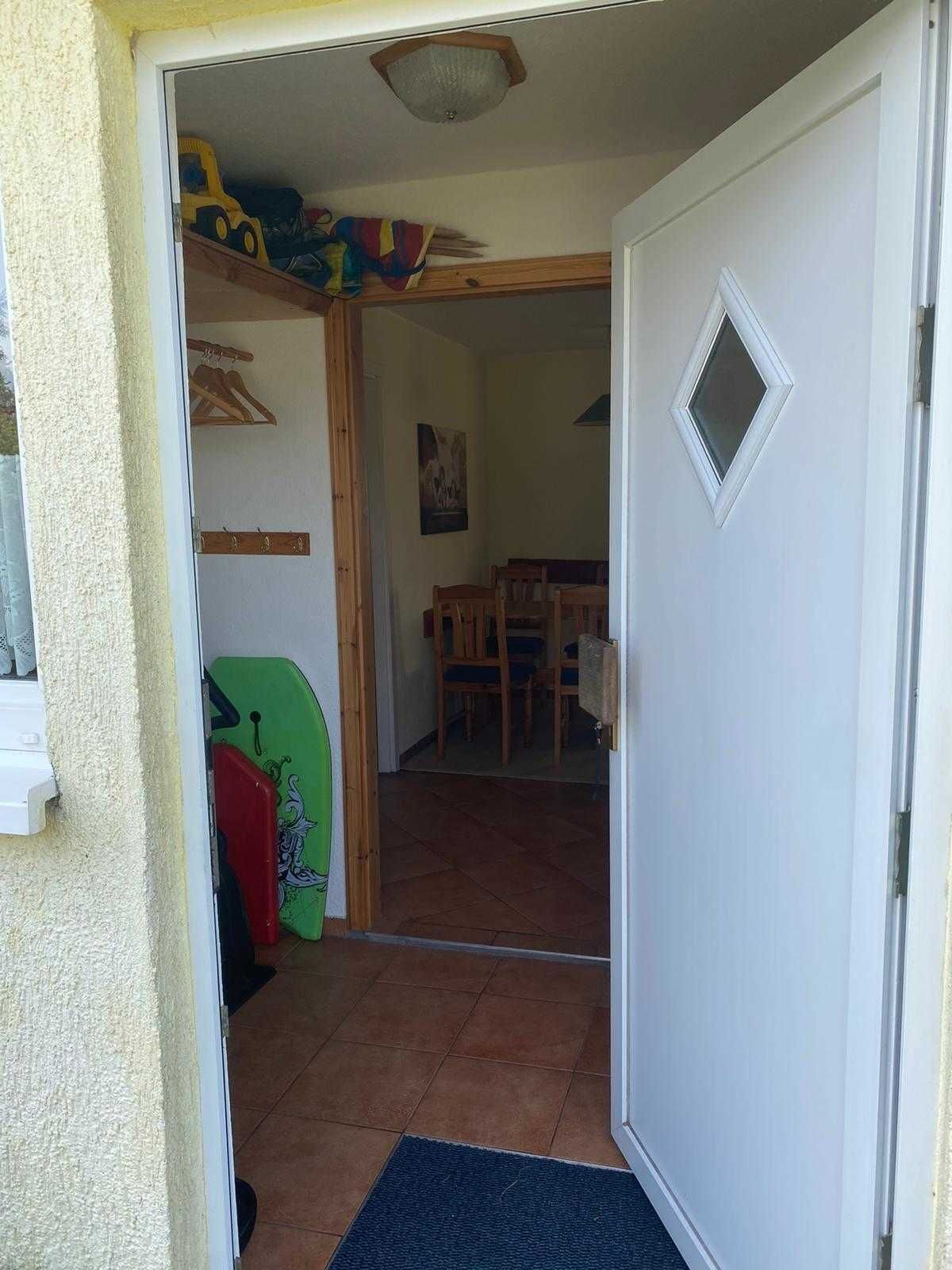 Ein Zimmer mit Fliesenboden, einer Holztür, einem kleinen Fenster und einem Essbereich mit Stühlen und einem Tisch.