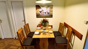 Un coin repas avec une table en bois, quatre chaises, un vase de fleurs et un tableau accroché au mur.