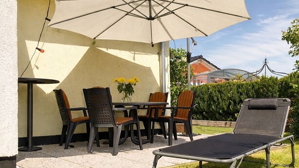 Une terrasse extérieure avec une table et des chaises, un transat et un grand parasol.