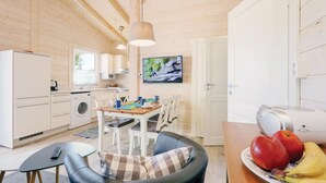 Una cocina moderna con paredes de madera, un comedor con mesa y sillas, un televisor montado en la pared y un frutero sobre la mesa.