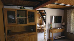 Un interior de madera con comedor, televisor y escalera.