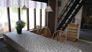 Un comedor con una mesa cubierta con mantel floreado, sillas de madera y una planta en maceta con flores.