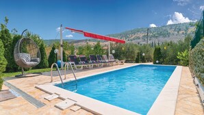 Piscina rectangular con borde de piedra, rodeada de sillas de descanso y una silla colgante.