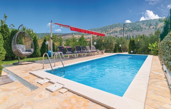 A rectangular swimming pool with a stone border, surrounded by lounge chairs and a hanging chair.