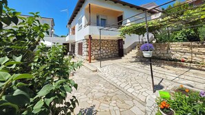 A two-story house with a stone facade, a tiled patio, and a garden with flowers. - Holiday apartment 100 m from the beach (Crikvenica)