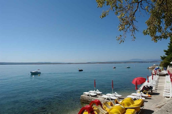 A calm lake with boats, a row of sun loungers, and a clear sky.