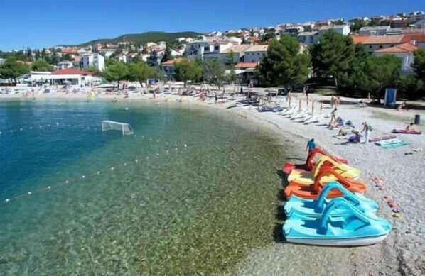 A beach with clear water, a row of colorful inflatable boats, and a row of umbrellas.