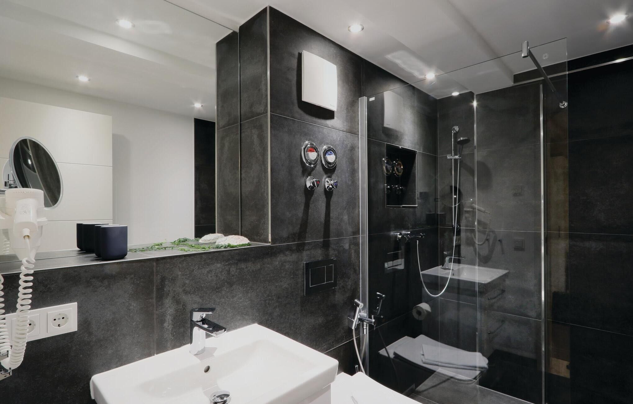 Un baño moderno con un espejo grande, un lavamanos blanco, una ducha con cerramiento de vidrio y un inodoro.