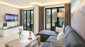 Une chambre d’hôtel moderne équipée d’une télévision à écran plat, d’une table basse en bois, d’un canapé et d’une grande fenêtre donnant sur l’extérieur.