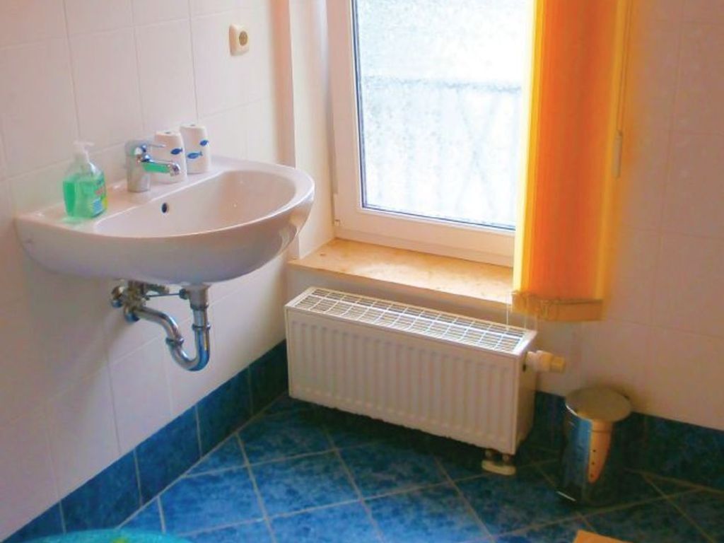 A bathroom with a white sink, blue tiles, a window with a view, and a radiator.