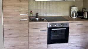 A modern kitchen with wooden cabinetry, a stainless steel sink, a built-in oven, and a coffee maker.