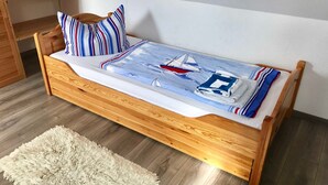 A wooden bed with a sailboat design bedspread, pillows, and a fluffy rug.
