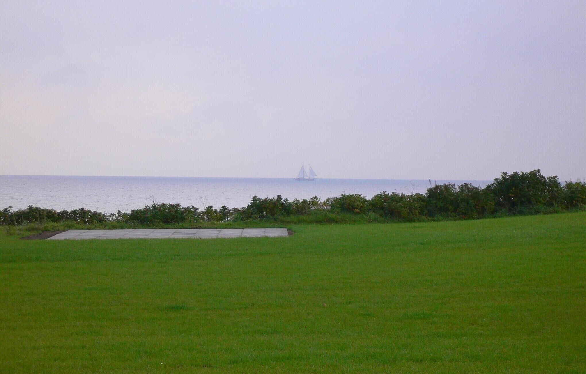 A grassy field with a body of water and a sailboat in the distance.