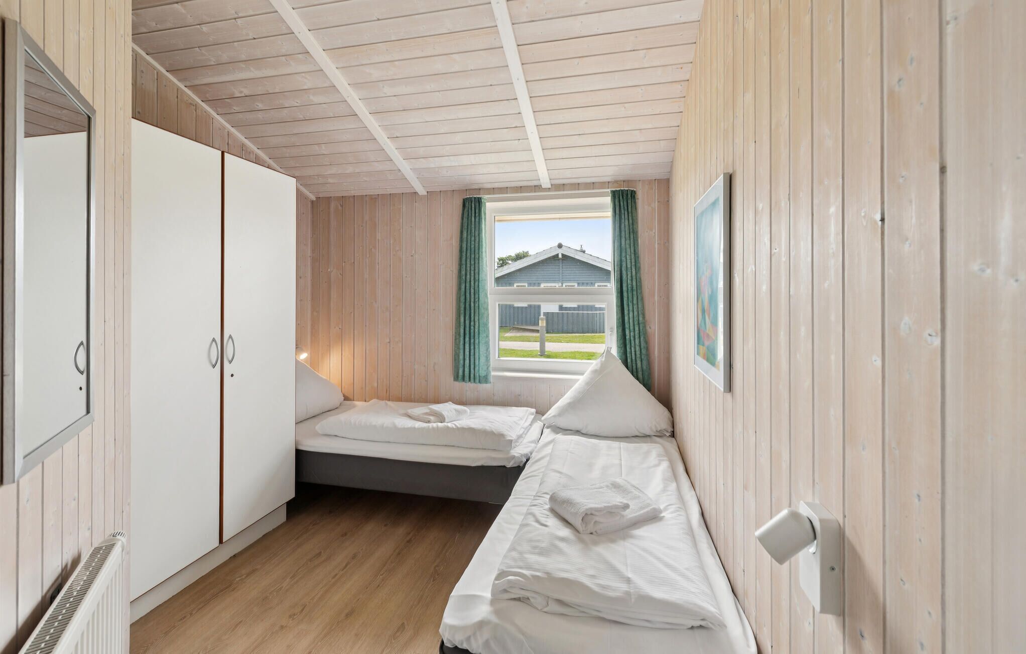 A compact room with two beds, a wardrobe, a radiator, and a window with curtains.