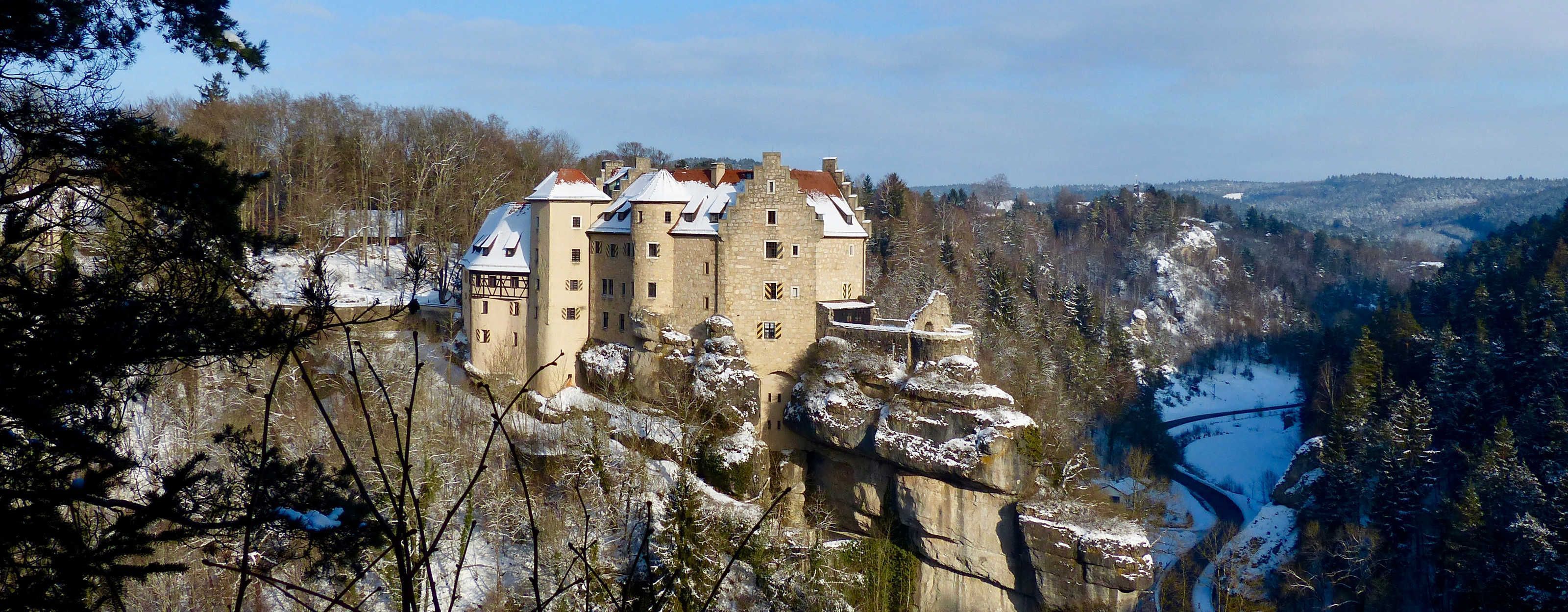 A castle with multiple towers, situated on a cliff overlooking a river.