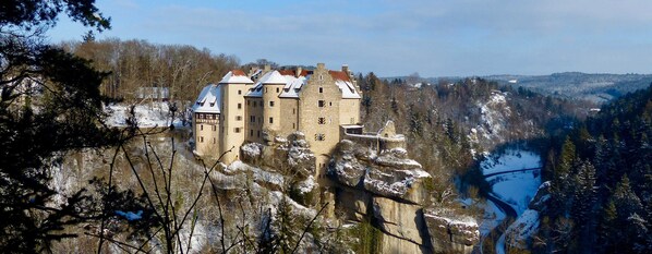 Een kasteel met meerdere torens, gelegen op een klif met uitzicht op een rivier.
