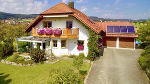 Una casa de dos pisos con techo inclinado, un balcón con jardineras, un porche cubierto y un garaje con paneles solares.