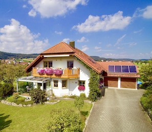 Una casa de dos pisos con techo inclinado, un balcón con jardineras, un porche cubierto y un garaje con paneles solares.