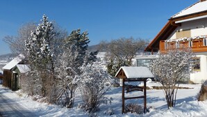 A snow-covered landscape with a wooden sign indicating a lodging area, surrounded by snow-laden trees and a building with a sloped roof. - Apartment White - Apartment Zut (Ahorntal)