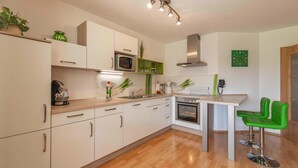 Una cocina moderna con armarios blancos, un microondas, un horno, un fregadero y un taburete verde.