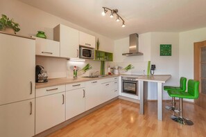Una cocina moderna con armarios blancos, un microondas, un horno, un fregadero y un taburete verde.