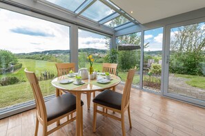 Un espace repas avec un mur en verre, des chaises en bois, une table ronde et une vue sur un paysage verdoyant.