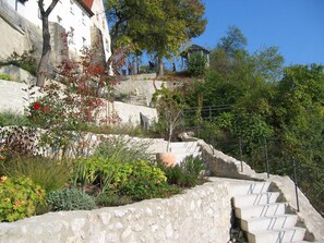 Un escalier en pierre mène à un bâtiment à la façade blanche, entouré de verdure et d’arbres.