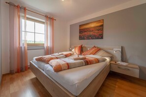 Une chambre à coucher avec un grand lit, une table de chevet, une fenêtre avec des rideaux et un tableau au mur.