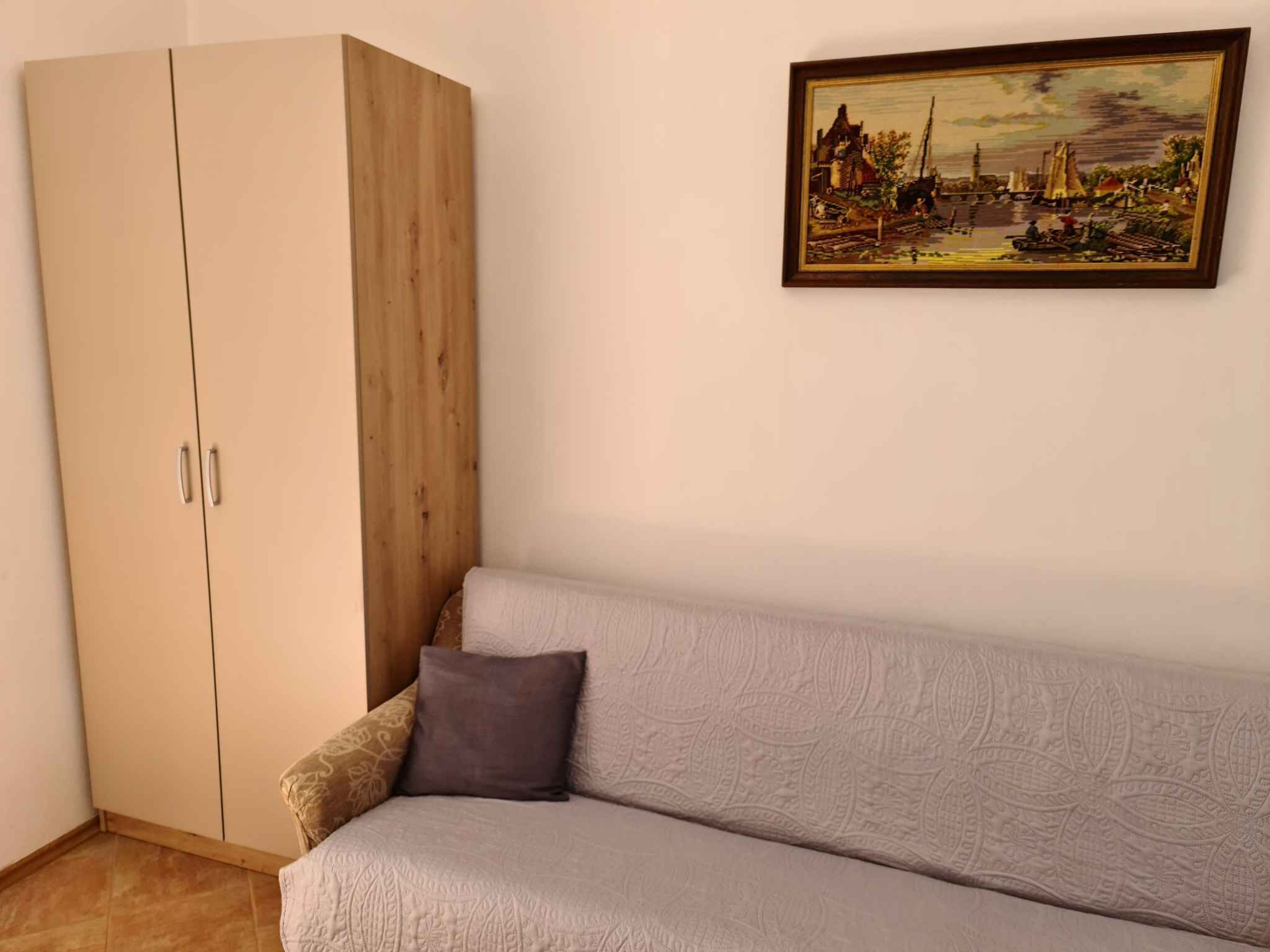 A room with a beige sofa, a wooden wardrobe, and a framed painting on the wall.