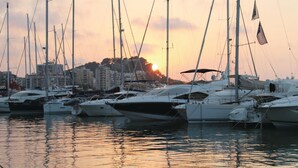 Un port de plaisance où sont amarrés de nombreux voiliers, avec une vue sur la ville en arrière-plan et un coucher de soleil.