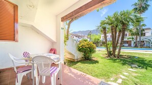Une terrasse avec une table et des chaises, un petit jardin agrémenté de palmiers et, au loin, une vue sur une chaîne de montagnes.