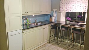 A kitchen with white cabinets, a sink, and a window with a floral curtain. - Gorgeous home in Vågstranda with house sea view (Vågstranda)