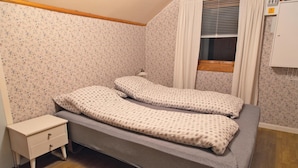 A small, single-bed room with floral wallpaper, a wooden headboard, a bedside table, and a window with blinds. - Gorgeous home in Vågstranda with house sea view (Vågstranda)