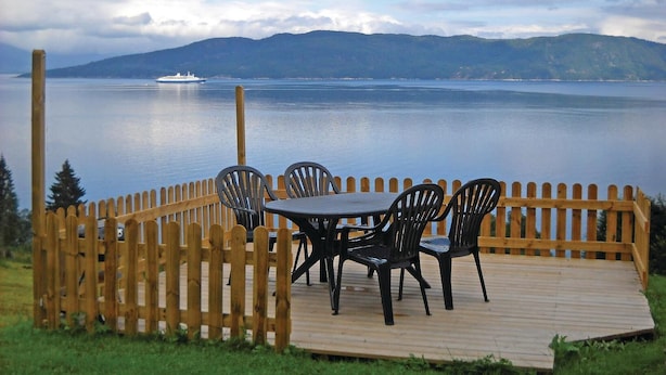 A wooden deck with a table and chairs overlooking a calm body of water with a ship in the distance and mountains in the background. - Gorgeous home in Vågstranda with house sea view (Vågstranda)
