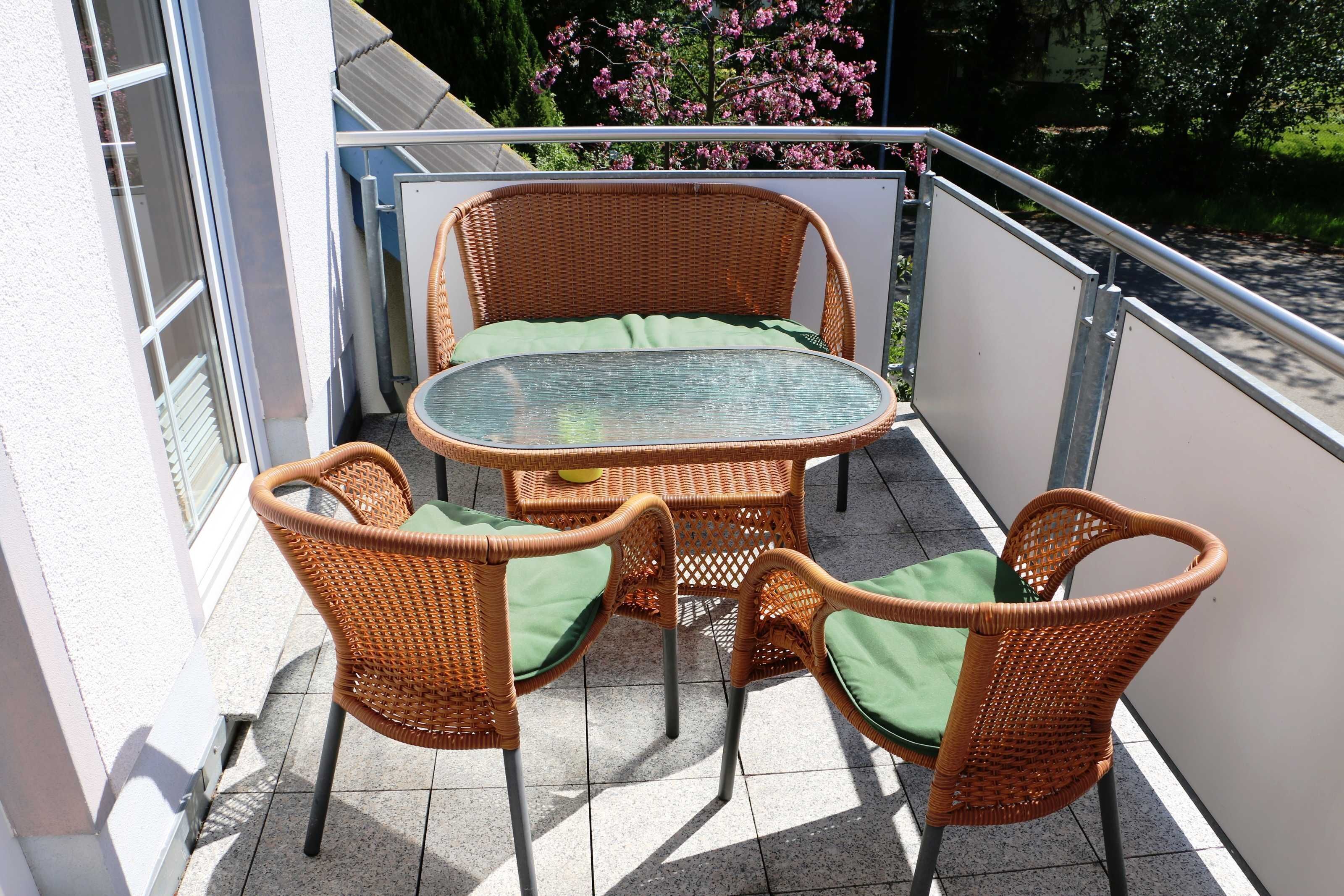 A balcony with wicker furniture, including a table and chairs, and a glass-top table.