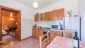 A compact kitchen with wooden cabinets, a microwave, a stove, and a refrigerator. There is a dining table with a floral tablecloth and chairs. - 1 bedroom gorgeous apartment in Rabac (Rabac)