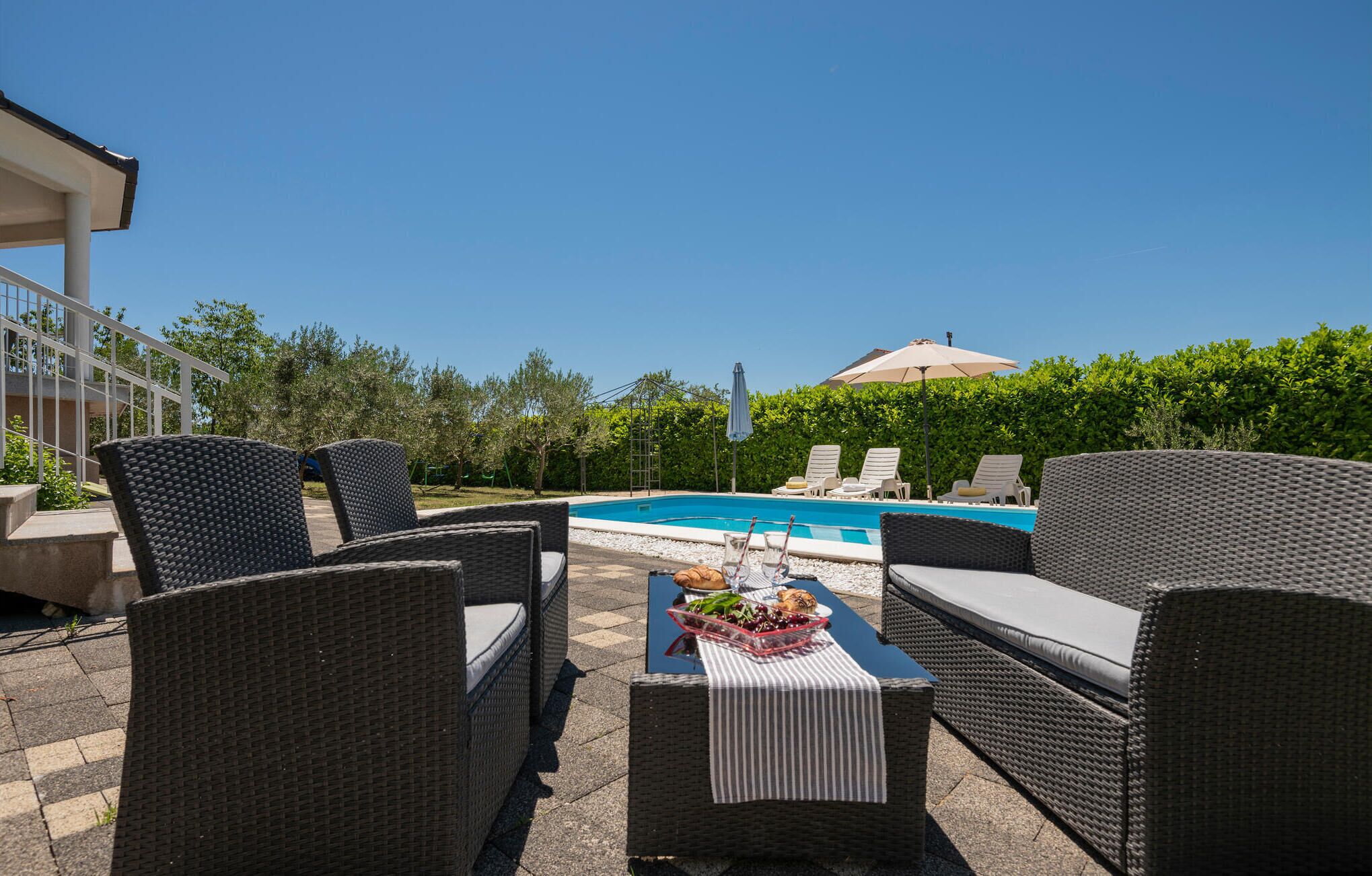 An outdoor patio with wicker furniture, a pool, and a view of a building in the background.